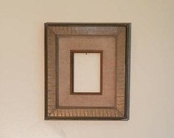 May include: A simple, rectangular picture frame with a light brown wood finish. The frame has a raised edge and a slightly textured surface. The frame is empty and ready for a photo or artwork.