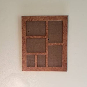 May include: A multi-photo frame with a wood-grain finish. The frame has six openings of varying sizes, arranged in a rectangular shape. The frame is mounted on a light-colored wall.