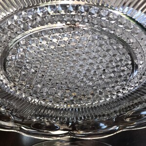 May include: A clear glass serving plate with a raised, textured design. The plate has a scalloped edge and a center that is slightly indented.