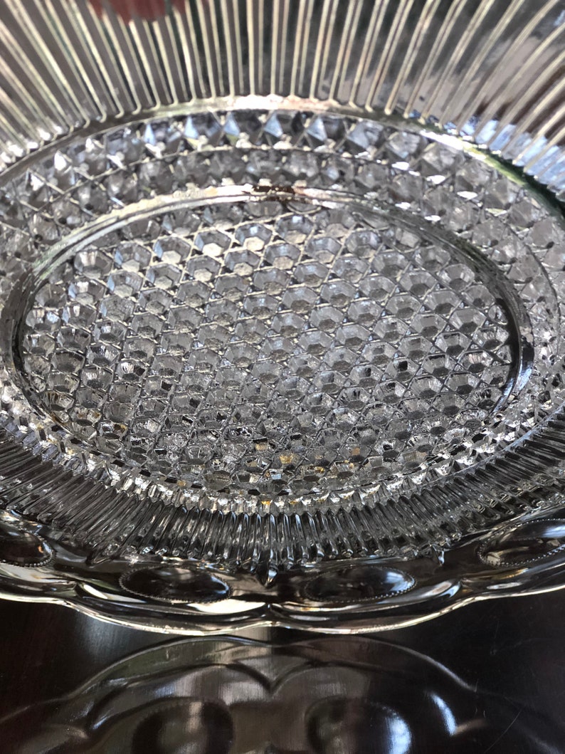May include: A clear glass serving plate with a raised, textured design. The plate has a scalloped edge and a center that is slightly indented.