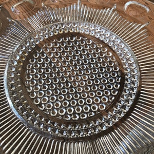 May include: A clear glass serving dish with a raised, textured design. The center of the dish has a honeycomb pattern, and the outer edge has a scalloped design.