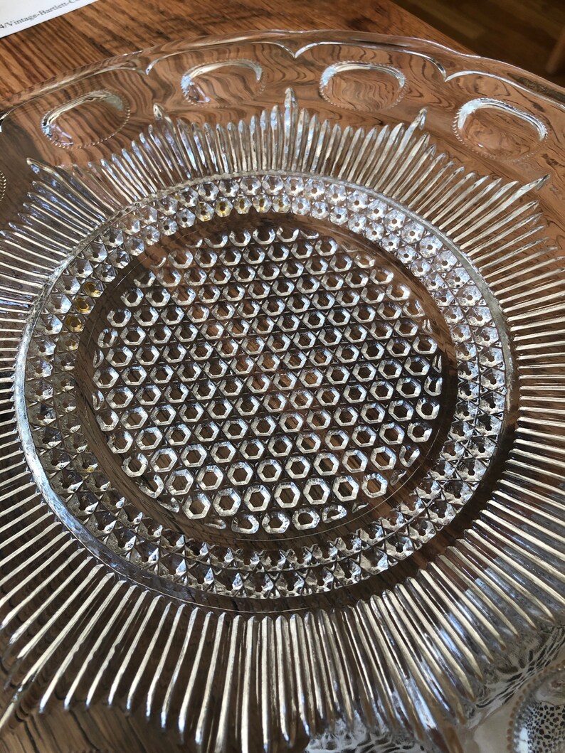 May include: A clear glass serving dish with a raised, textured design. The center of the dish has a honeycomb pattern, and the outer edge has a scalloped design.