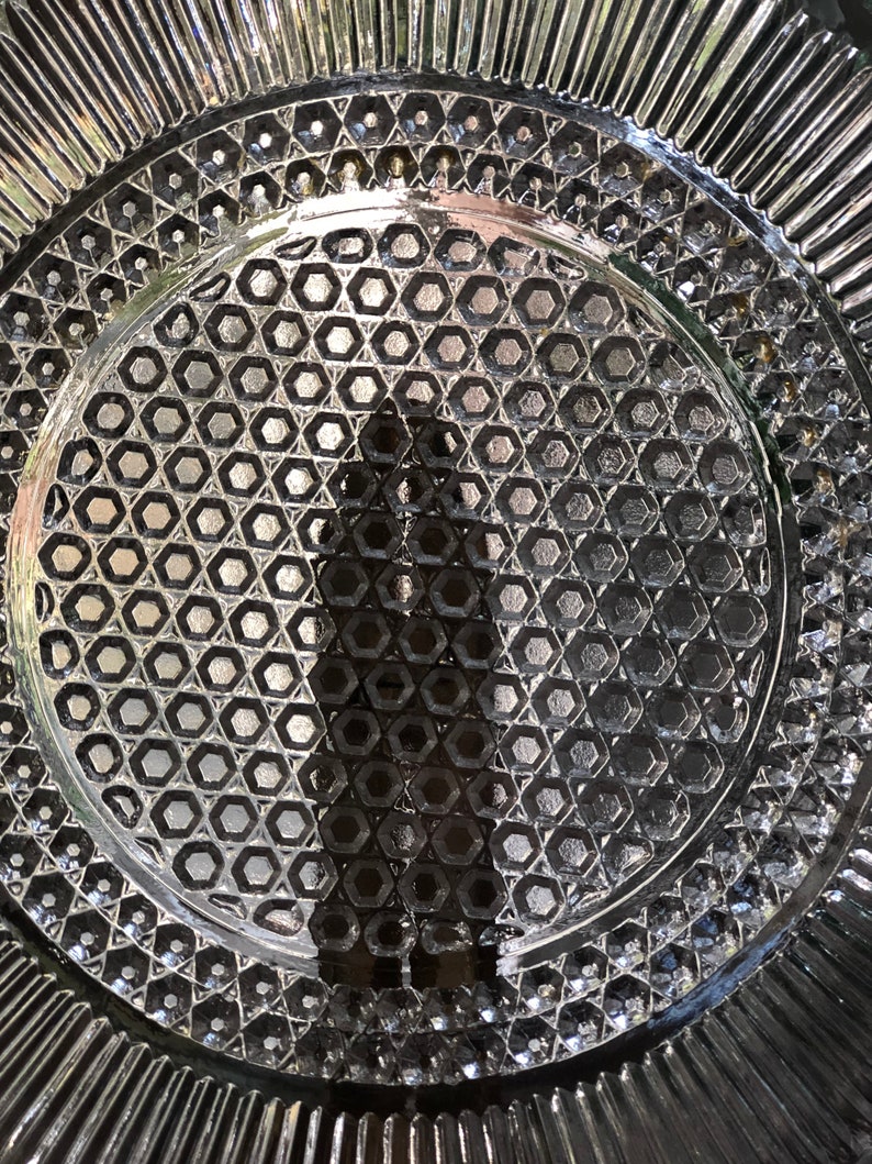 May include: A clear glass plate with a decorative hexagonal pattern. The plate has a scalloped edge.
