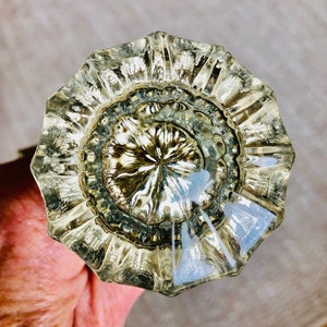 May include: A clear, faceted glass doorknob with an octagonal shape. The knob has a detailed, textured surface with radial patterns and a central floral design. The glass reflects light, creating highlights and shadows.