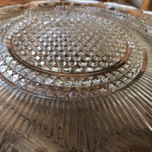 May include: A clear glass plate with a diamond pattern and a raised edge. The plate has a textured surface and a slightly scalloped edge.
