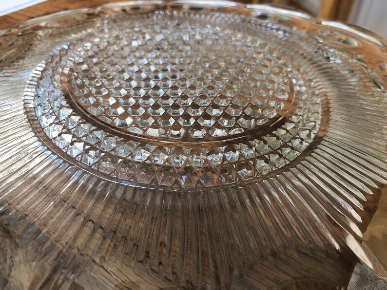 May include: A clear glass plate with a diamond pattern and a raised edge. The plate has a textured surface and a slightly scalloped edge.