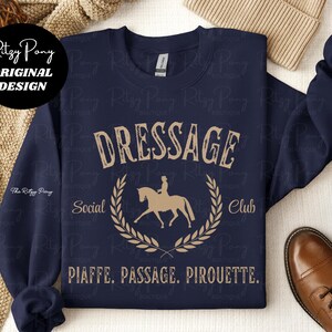 Pu&ograve; includere: Felpa blu navy con scritta beige "DRESSAGE Social Club" e grafica di cavallo e cavaliere. Il testo "PIAFFE. PASSAGE. PIROUETTE." &egrave; sotto. Design originale di Ritzy Pony.