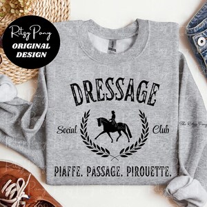 Pu&ograve; includere: Una felpa grigio melange con la scritta nera "DRESSAGE Social Club". Una silhouette nera di un cavallo e un cavaliere &egrave; centrata sotto la parola "DRESSAGE". Le parole "PIAFFE. PASSAGE. PIROUETTE." sono stampate sotto.