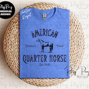 May include: A blue heather t-shirt with a graphic design featuring the words "AMERICAN QUARTER HORSE" and a horse silhouette. The text "America's Breed" and "Est. 1940" are also included. The shirt has a crew neck.
