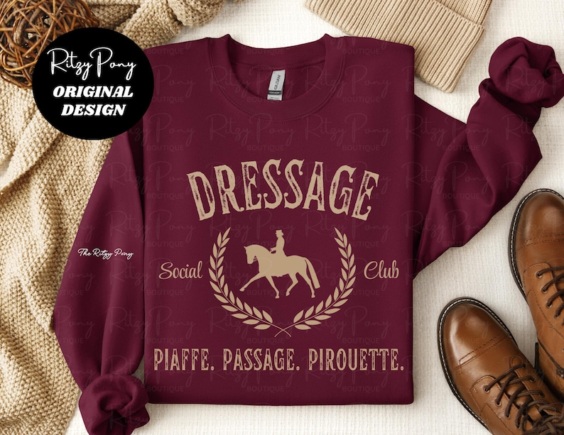 Pu&ograve; includere: Felpa bordeaux con la scritta "DRESSAGE Social Club" in stile vintage. Il design include una silhouette di cavallo e cavaliere all'interno di una corona d'alloro. Le parole "PIAFFE. PASSAGE. PIROUETTE." sono stampate sotto.