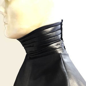 May include: A black leather collar with a pleated design. The collar is folded down and has a smooth, shiny finish.