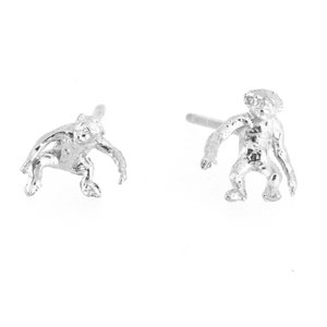 Puede incluir: Un par de pendientes de plata con un pequeño diseño de mono detallado. El mono está representado en posición de cuclillas con los brazos extendidos.