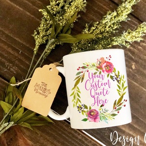 K&ouml;nnte beinhalten: Ein wei&szlig;er Keramikbecher mit einer bunten Blumenkranz-Grafik, die den violetten Text "Your Custom Quote Here" umgibt. Ein braunes Papieretikett mit der Aufschrift "The Mug Mommy" ist mit einer Schnur am Henkel befestigt.