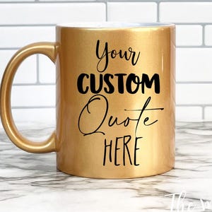 May include: A metallic gold ceramic mug with a curved handle. The front of the mug features black text that reads Your CUSTOM Quote HERE in a combination of bold block lettering and a cursive script font style.