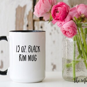 May include: A white ceramic mug with a black handle and black rim. The text 15 oz. Black Rim Mug is printed in black on the front of the mug. The mug has a cylindrical body and a curved handle, providing a clear view of the product's design.