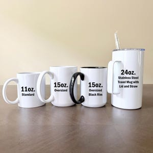 K&ouml;nnte beinhalten: Vier wei&szlig;e Tassen in verschiedenen Gr&ouml;&szlig;en und Ausf&uuml;hrungen. Von links nach rechts: eine 11oz Standardtasse, eine 15oz gro&szlig;e Tasse, eine 15oz gro&szlig;e Tasse mit schwarzem Rand und Henkel sowie ein 24oz Edelstahl-Reisebecher mit Deckel und Trinkhalm.