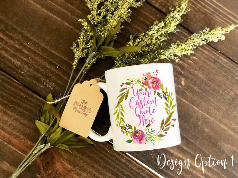 K&ouml;nnte beinhalten: Ein wei&szlig;er Keramikbecher mit einer bunten Blumenkranz-Grafik, die den violetten Text "Your Custom Quote Here" umgibt. Ein braunes Papieretikett mit der Aufschrift "The Mug Mommy" ist mit einer Schnur am Henkel befestigt.