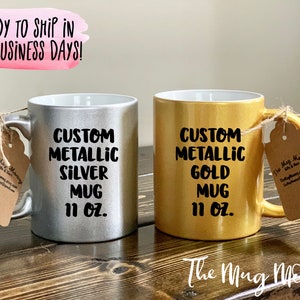 May include: Two metallic mugs, one silver and one gold, each with a handle and a tag. The silver mug reads "CUSTOM METALLIC SILVER MUG 11 OZ." The gold mug reads "CUSTOM METALLIC GOLD MUG 11 OZ."