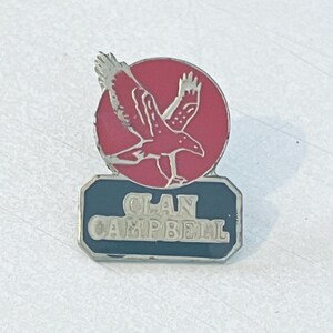 Puede incluir: Un pin vintage del Clan Campbell. El pin presenta un águila roja en vuelo contra un círculo rojo, con las palabras "Clan Campbell" en letras blancas sobre una base rectangular azul. El pin tiene un borde plateado.