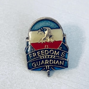 Puede incluir: Pin metálico con diseño patriótico. El pin presenta un águila dorada y el texto "FREEDOM'S GUARDIAN" en letras azules. El pin tiene una combinación de colores azul, blanco y rojo.