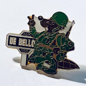 May include: A vintage pin depicting a cartoon beaver in military attire, pointing upwards. The beaver is wearing a green helmet and camouflage. The pin includes a sign that reads "DE BELLO" and "1990". The pin has gold-coloured edges.