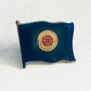 May include: A blue enamel pin with a gold and red emblem. The emblem features a stylized globe with a red band and the text "WORLD ECONOMIC FORUM".