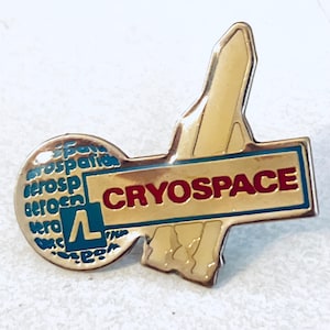 May include: A gold-colored pin with the word "CRYOSPACE" in red letters on a blue background. The pin has a stylized shape with a rocket and a circular element with the word "aerospace" in blue.