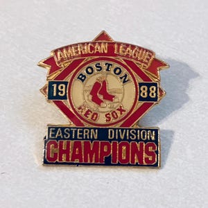 May include: A vintage Boston Red Sox pin with the team logo, red socks, and the words "Boston Red Sox" and "American League". The pin also displays "1988 Eastern Division Champions" in red and gold.