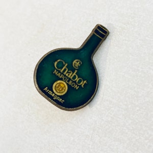 May include: A green and gold metal pin shaped like a bottle of Chabot Napoleon Armagnac.
