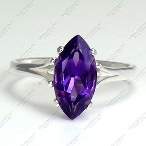 May include: A silver ring featuring a marquise-cut, deep purple amethyst gemstone. The gemstone is set with four prongs, and the band has a split design. The ring is displayed on a white background.
