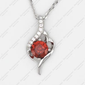 Può includere: Una collana con ciondolo in argento con una pietra rossa circondata da pietre bianche più piccole. Il ciondolo ha la forma di una fiamma stilizzata.