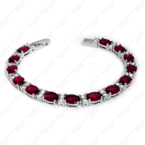 Puede incluir: Un brazalete de plata con una fila de piedras preciosas rojas ovaladas y piedras preciosas transparentes más pequeñas.