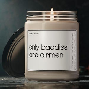 May include: A lit beige candle in a glass jar with a black lid. The label reads "only baddies are airmen". The candle is from Kizzybel Designs.