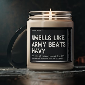May include: A black and white candle with a label that reads "Smells Like Army Beats Navy" and "the aroma of victory, crafted from 100% success and a subtle hint of triumph."
