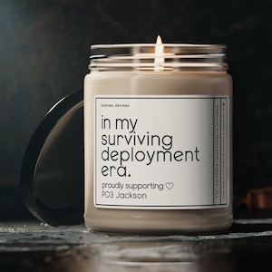 May include: A beige candle with a white label that reads "in my surviving deployment era. proudly supporting PO3 Jackson".