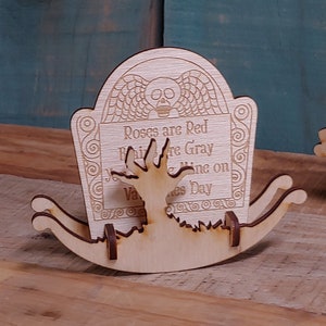 May include: A wooden tombstone with a skull and wings design. The tombstone says "Roses are Red, Violets are Gray, I'll be your Valentine on Valentine's Day".