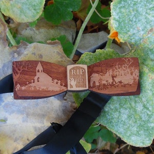 May include: A wooden bow tie with a spooky Halloween design. The bow tie features a church, a graveyard, and a tombstone that reads "RIP Here Lies Fred Dead".