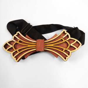 Könnte beinhalten: Ein Holz-Fliege mit einem geometrischen Design in Braun- und Goldtönen. Die Fliege ist an einem schwarzen verstellbaren Band befestigt.