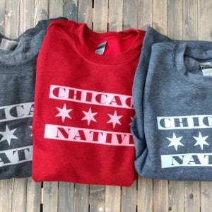 May include: Three sweatshirts with the text "Chicago Native" and six white stars on a red, gray, and dark gray background.