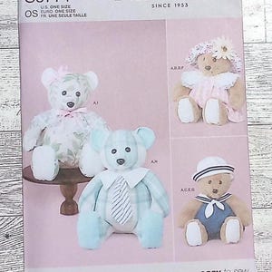 May include: A sewing pattern featuring four teddy bear designs. The bears are shown in various outfits, including a floral dress, a sailor suit, and a tie. The pattern is labeled "Laura Ashley" and "Simplicity".