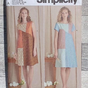 May include: Simplicity sewing pattern number S9615 for a dress with two different styles. The first style is sleeveless with a geometric pattern in orange, brown, and white. The second style has short sleeves and a geometric pattern in blue, pink, and white. Both styles are knee-length.