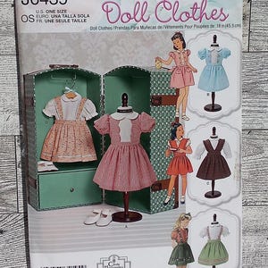May include: Simplicity pattern J0439 for doll clothes. The pattern includes five different outfits for 18-inch dolls. The outfits include a pink and white dress, a red and white dress, a blue dress, a brown dress, and a green dress with a white apron.