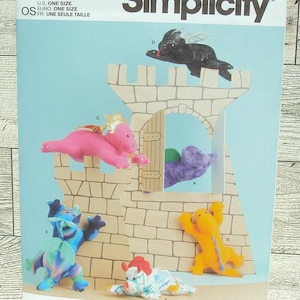 May include: Simplicity sewing pattern S9876 featuring plush toy dragons. The pattern includes instructions for creating various colorful dragon designs, with a castle backdrop. The pattern is designed and printed in the USA.