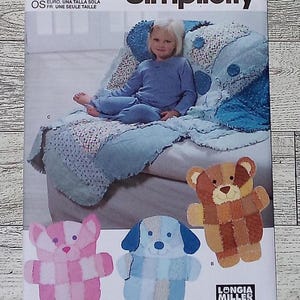 May include: Simplicity sewing pattern S9674 featuring a child's quilt and stuffed animal designs. The pattern includes a child wearing blue pajamas on a blue quilt. Three stuffed animal designs are shown: a pink bear, a blue dog, and a brown bear.