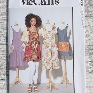 May include: McCall's sewing pattern M8308 featuring four apron designs. The pattern includes sizes A (S-M-L-XL). The image shows a woman wearing an apron. The pattern is designed and printed in the USA.