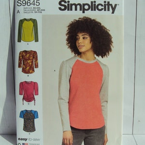 May include: Simplicity sewing pattern S9645 for a long-sleeved shirt with four different variations. The pattern includes a color image of a model wearing a red and grey shirt with a round neckline. The pattern is labeled "easy-to-sew" and "designed and printed in USA."