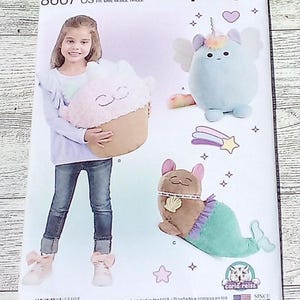May include: Simplicity pattern featuring plush toy designs. The pattern includes instructions for creating a cupcake-shaped plush, a winged unicorn plush, and a mermaid plush. The pattern is marked "US ONE SIZE" and "SINCE 1927".