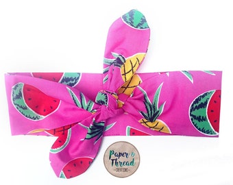 May include: Pink headband with a watermelon and pineapple print. The headband is tied in a knot at the top. The text "Paper & Thread - Creations" is on a small tag.
