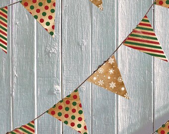 May include: A string of brown paper triangle flags with different holiday patterns. The patterns include red and green polka dots, red and green stripes, and white snowflakes on a brown background.
