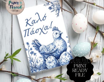May include: A white card with blue floral illustrations and Greek text, "Kalo Pascha!" features a blue hen and decorated Easter eggs. The card is surrounded by decorated Easter eggs and flowering branches, creating a festive Easter theme.